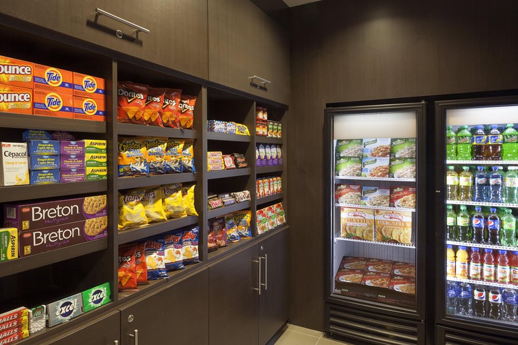 Mini fridge with drinks and snacks beside brown shelves with snacks
